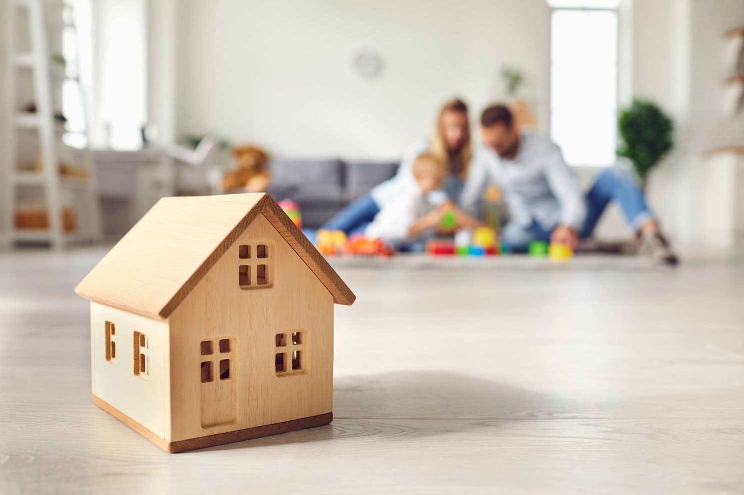 Wooden toy house with a family relaxing at home in the background